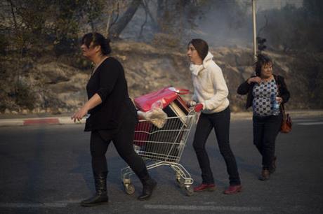 People carry their belongings inside a supermarket cart as they evacuate from wildfires in Haifa, Israel, Thursday, Nov. 24, 2016. A raging wildfire ripped through parts of Israel's third-largest city on Thursday, forcing tens of thousands of people to evacuate their homes and prompting a rare call-up of hundreds of military reservists to join overstretched police and firefighters. Spreading quickly due to dry, windy weather, the fire quickly spread through Haifa's northern neighborhoods. While there were no serious injuries, several dozen people were hospitalized for smoke inhalation. (AP Photo/Ariel Schalit)
