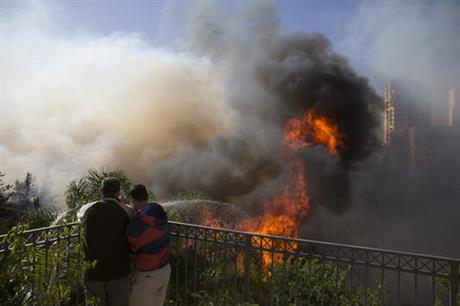 Men hose down wildfires in Haifa, Israel, Thursday, Nov. 24, 2016. Israeli police have arrested four Palestinians in connection with one of several large fires that damaged homes and prompted the evacuation of thousands of people in the past few days. Police are investigating the causes, including possible arson. Windy and hot weather have helped fan the flames. The blazes started three days ago near Jerusalem and in the north. Hundreds of homes were damaged. Russia, Italy and other countries are assisting the Israeli firefighters. (AP Photo/Ariel Schalit)