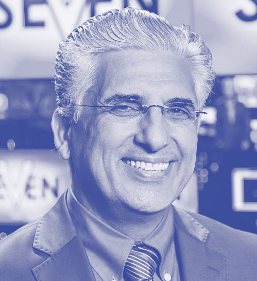 Smiling man in a suit and tie wearing glasses at a professional event.